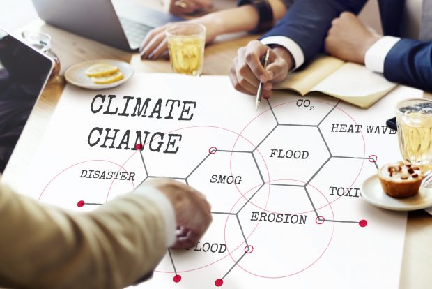 Two men seated, pointing at infographic placed on table, about climate change effects.