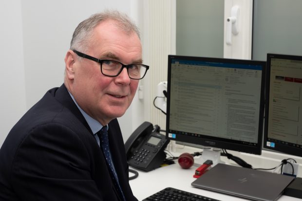 Martin Clarke, Government Actuary sitting at his desk in front of 2 screens and a phone. He has twisted round and faces the viewer.