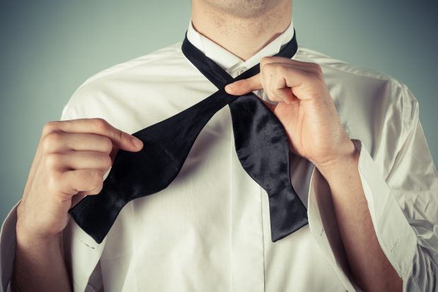 Man in white shirt tying black bow tie