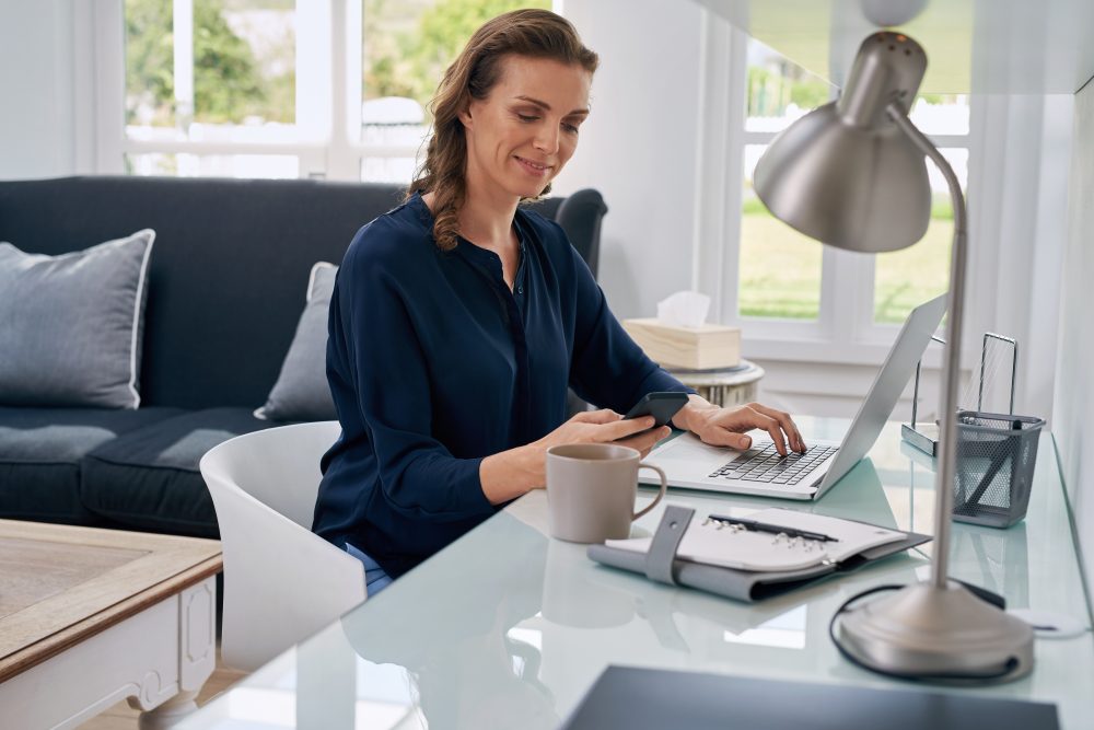 Woman with laptop looking at mobile phone.