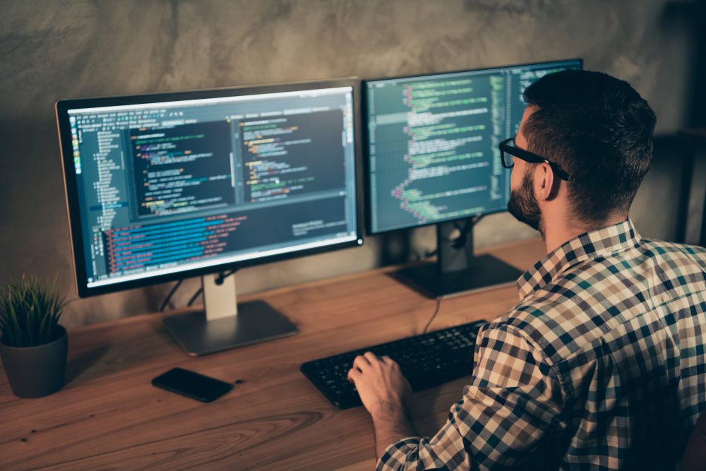 Computer programmer at a desk looking at 2 computer screens.