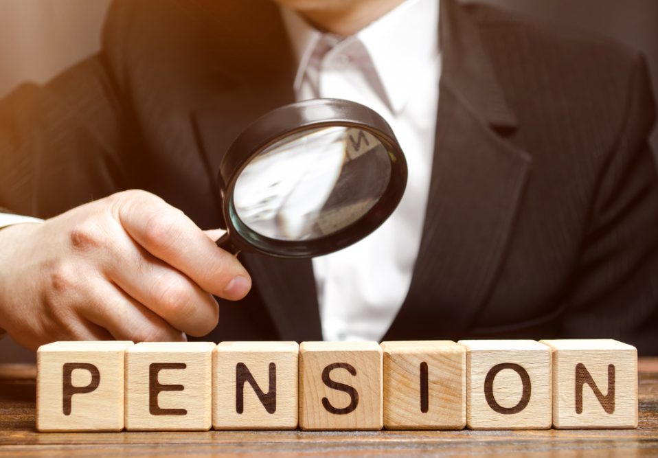 Man holding magifying glass looking at wooden blocks spelling out the word pension.