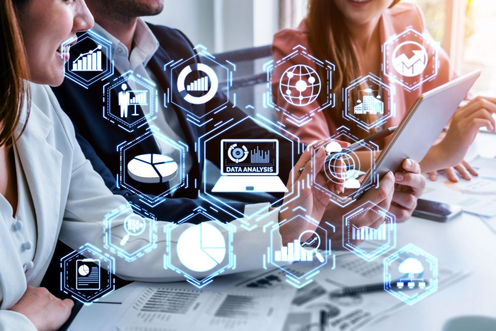 Image of 2 women and a man sitting at a table discussing various charts. Image overlaid with hexagonal shapes depicting internet icons.