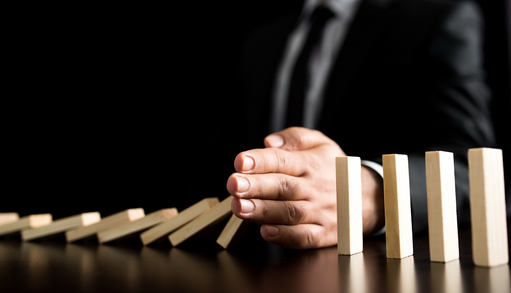 Man's hand stops dominoes from falling.