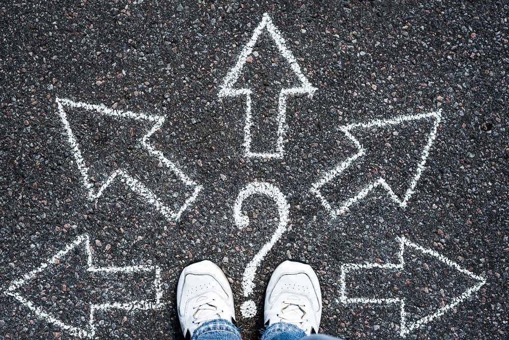 View of pair of trainers standing on tarmac on which threre are 5 arrows pointing in different directions.