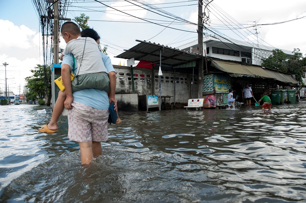 Woman carrying young boy on her back as she wades through flood waters.