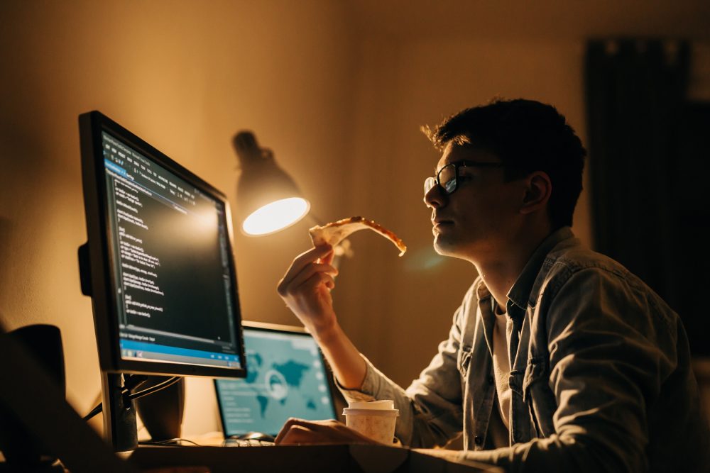 Man working at a computer at night by the light of a desktop lamp.