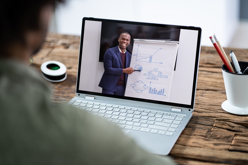 Man looking at laptop on which another man is teaching an online class.