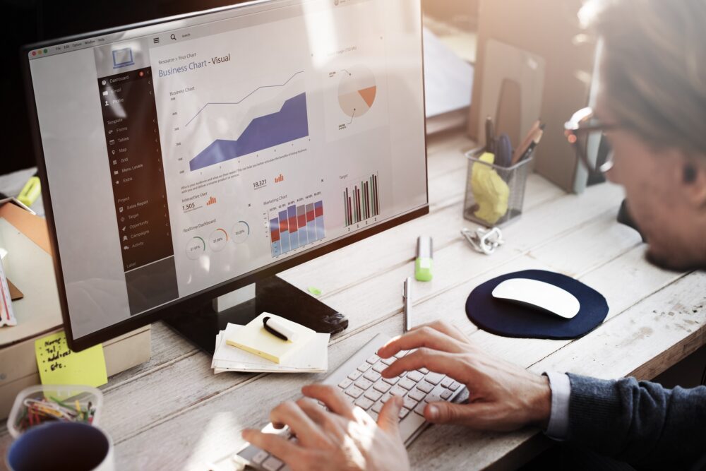 Man at computer looking at a business chart which shows bar charts and graphs.