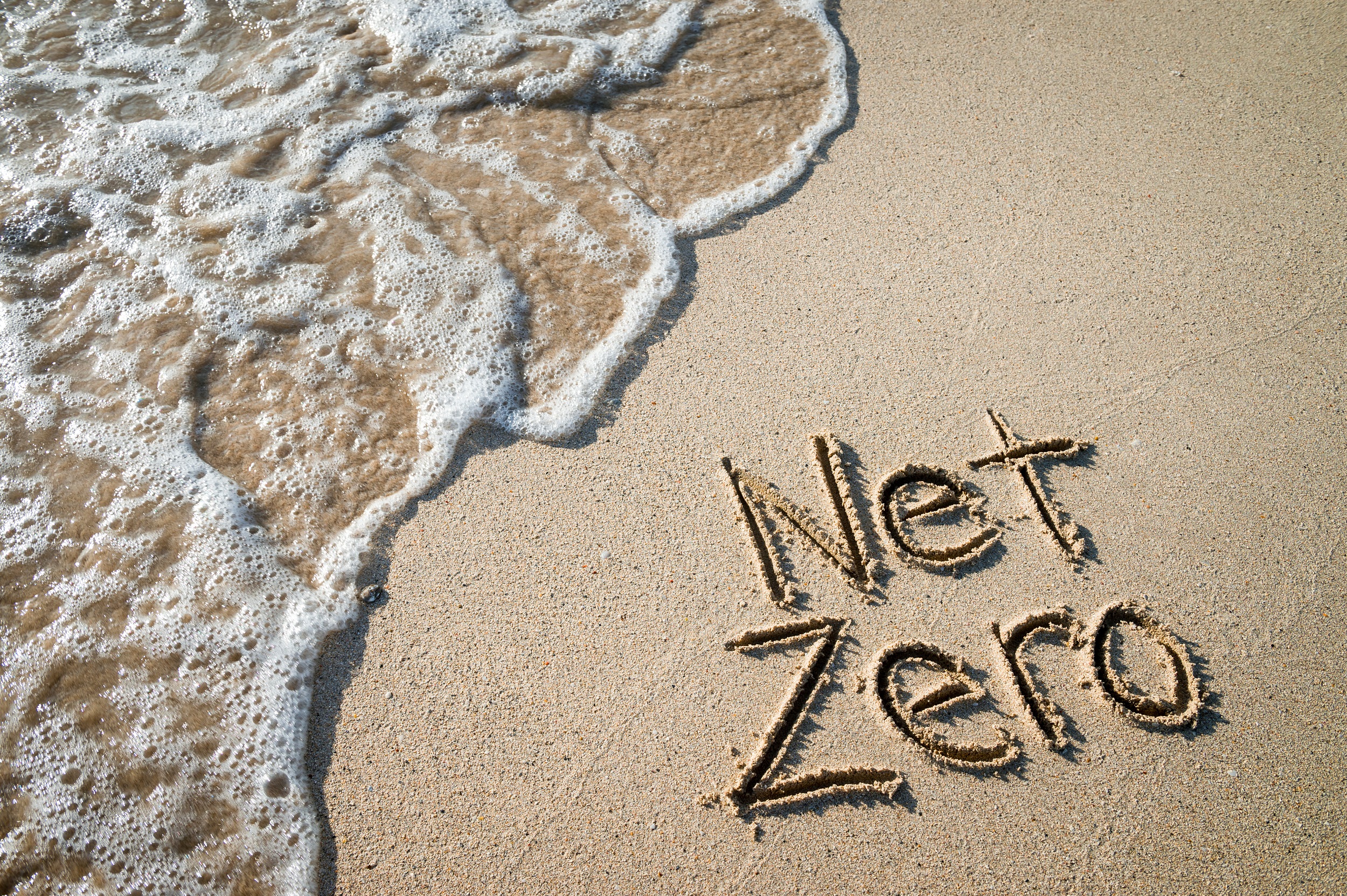 The words 'net zero' written in the sand of a beach.