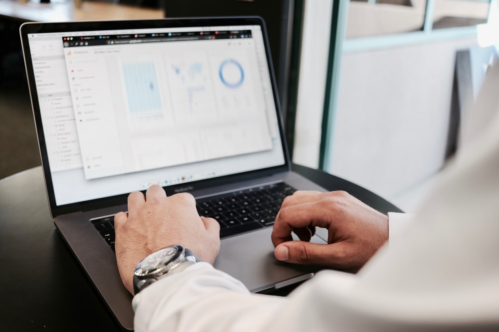 Man's hands on a laptop and on the screen is a blurred out information dashboard.