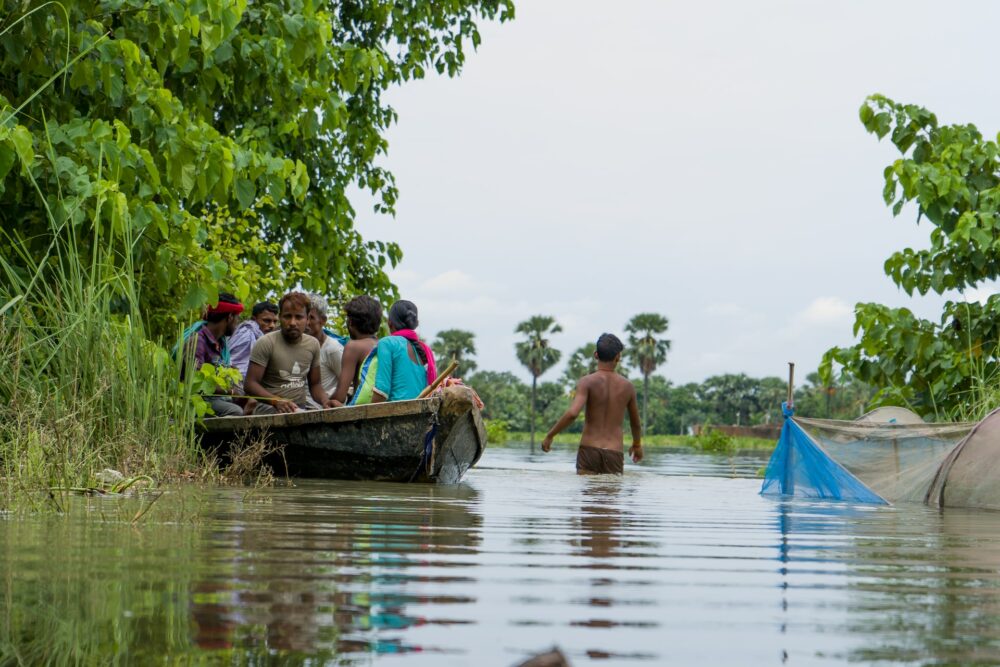 People in a canoe. There is a man in the centre of the image walking through the water.