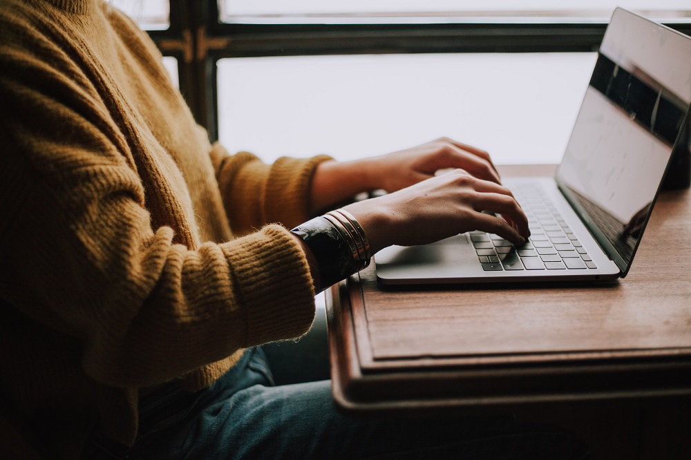 Torso of a person wearing a gold-coloured jumper typing on a laptop keyboard.