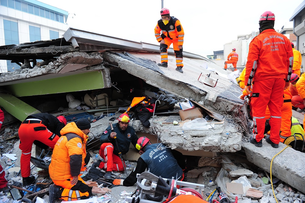 Rescuers wearing bright high-vis clothing and hard hats search the rubble of a building, following an earthquake.