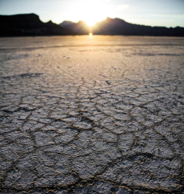 Close up of drought affected land. In the background of the image is the outline of a mountain range and the sun is setting behind one of the peaks.