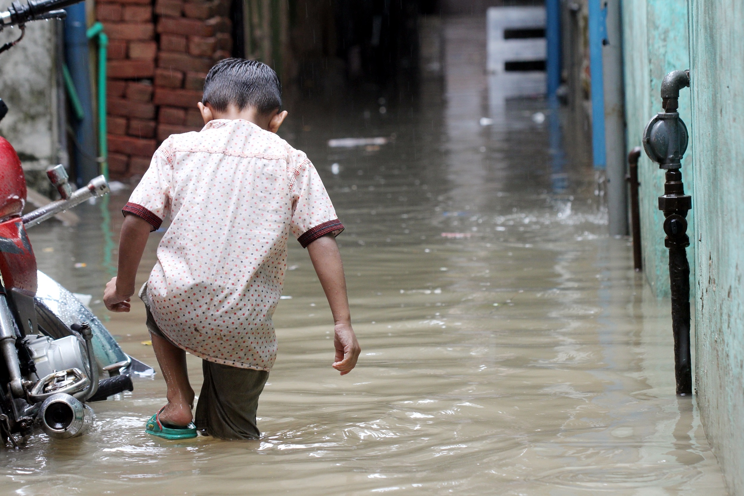 Rear view of a young boy stepping through floodwater in a street in Pakistan.