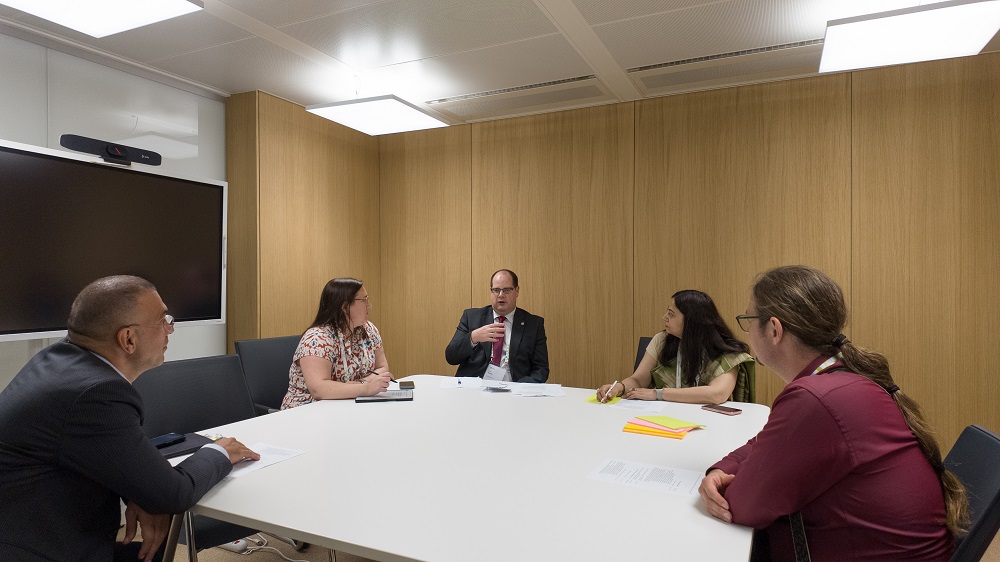 Five people sit around a white table in a small wooden pannelled conference room. One is GAD actuary Chris Morley who is gesturing with his right hand.