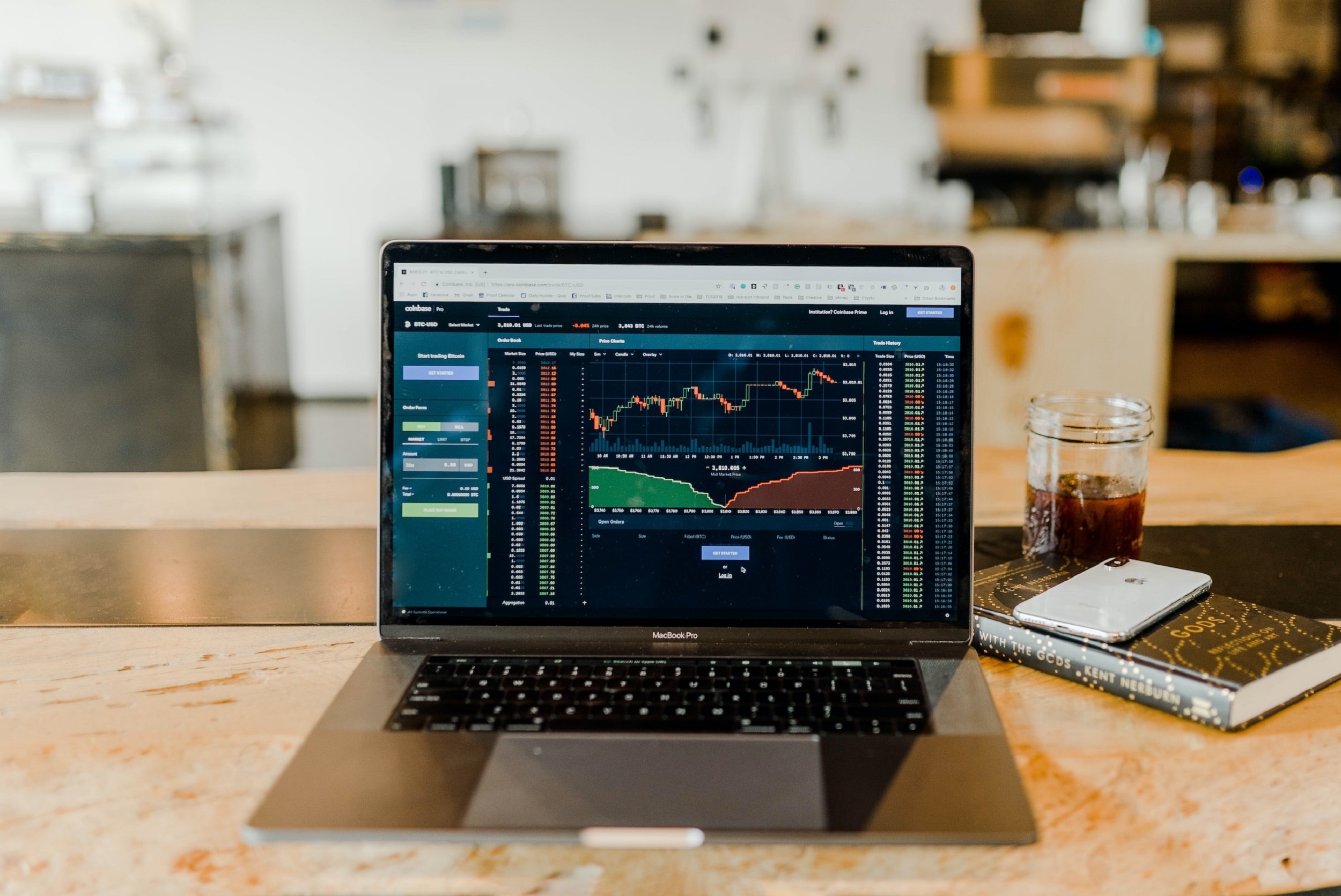 Laptop showing detailed graphs and other information in red and green. The computer is sitting on a marble table top and next to it is as notebook and phone. Credit: Unsplash.