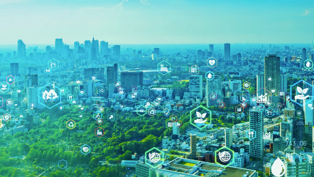 Bird's eye view of a city with green parks and high-rise buildings. There are icons depicting environmental ideas floating above each building. Credit: iStock.