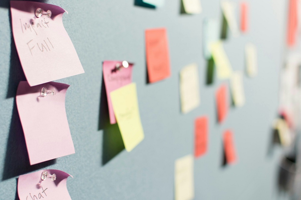 Close up of a grey felt board on which are placed several small, square post-it notes in a range of bright colours.