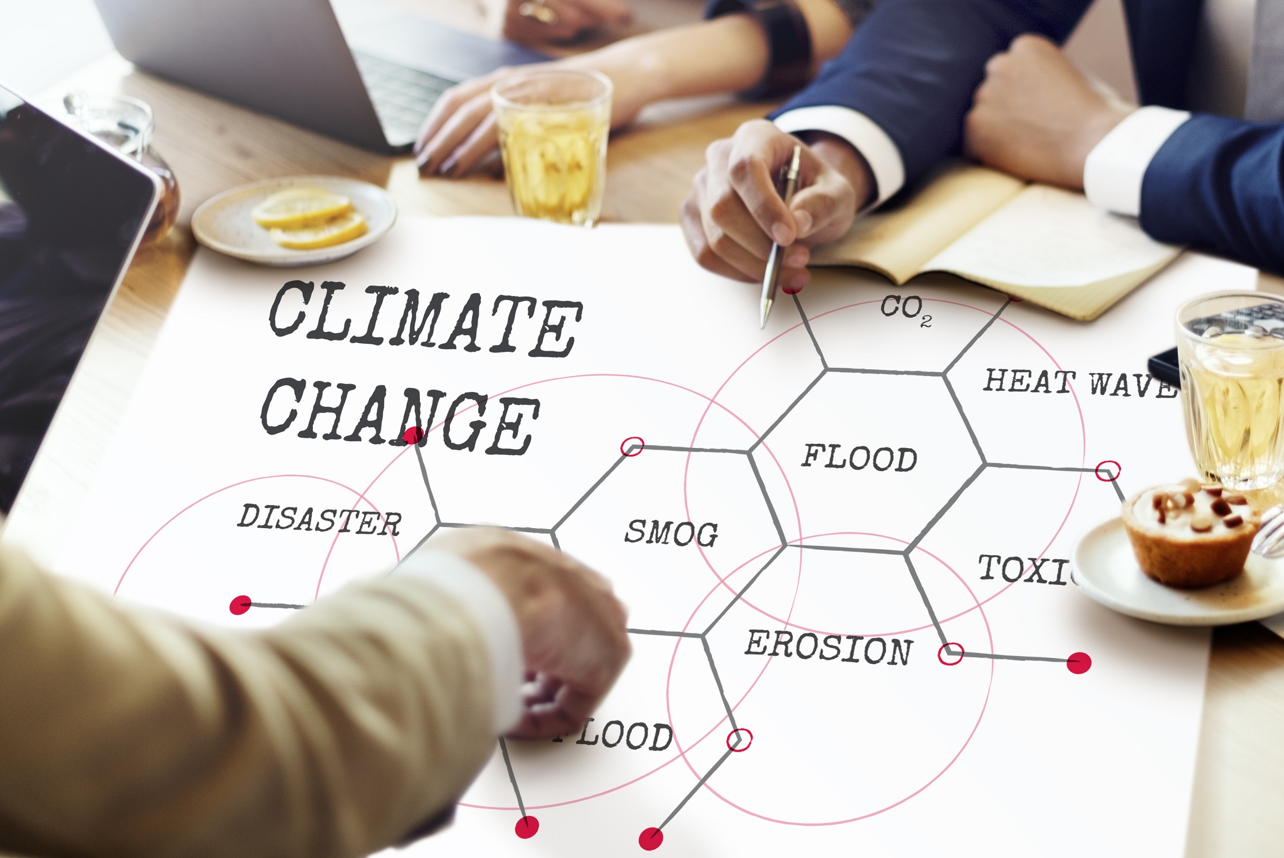 People sit at a table pointing to a large document on which is written the words climate change, flood, heat wave, erosion, smog, flood, toxic and disaster. Credit: Shutterstock