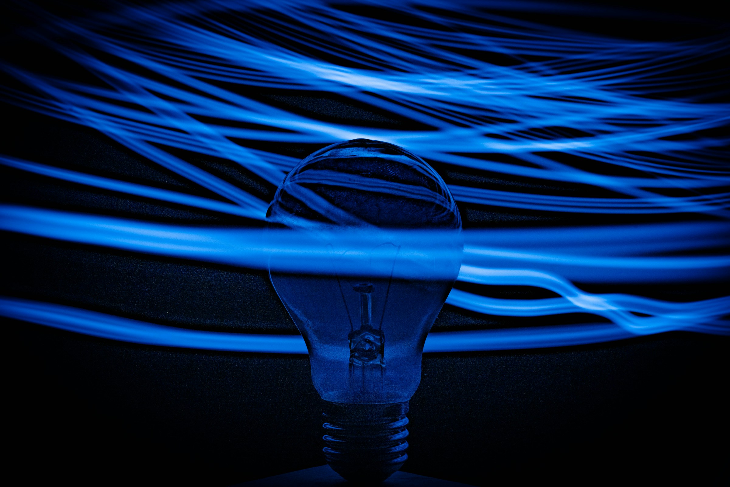 Unlit lightbulb pictured against a dark background, and surrounded by fluroescent blue lines. Credit: Unsplash