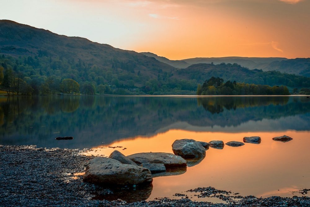 Brown rocks in a still lake with an orange sky, reflected in the water.