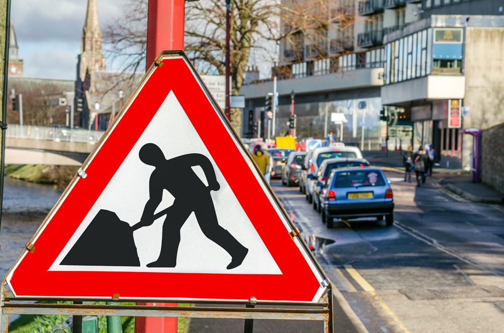Roadworks sign next to a row of cars waiting in the distance at a set of temporary traffic lights. Credit: Shutterstock