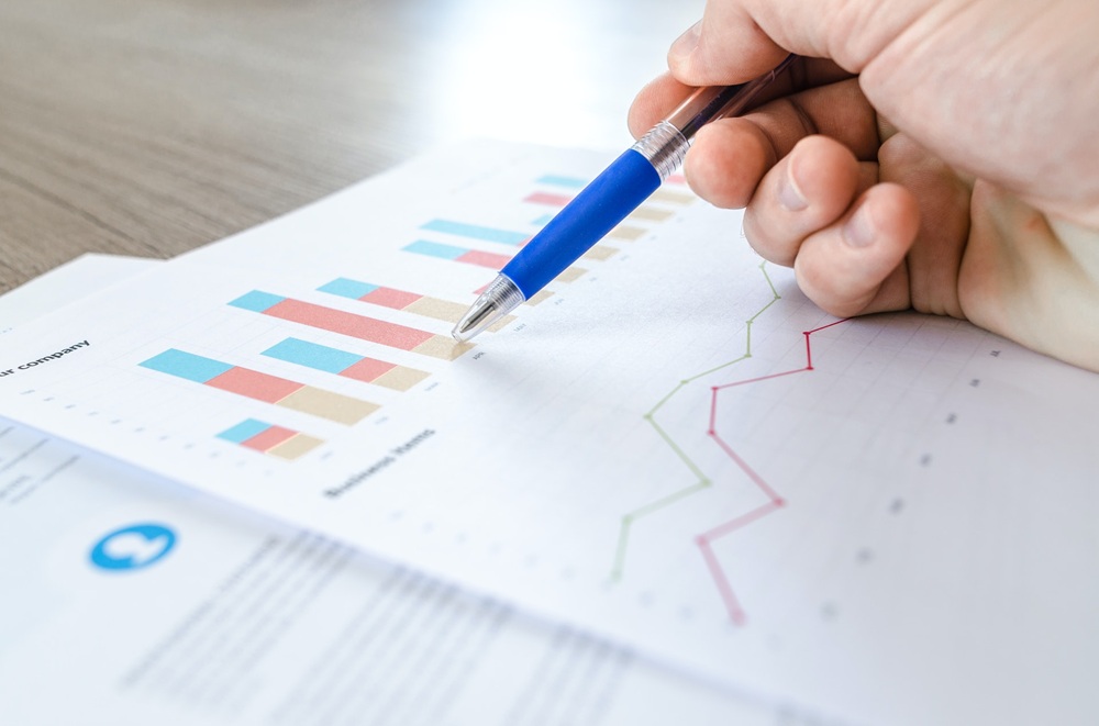 Close up of a person's hand holding a pen pointing to bar chart on paper. Credit: Unsplash
