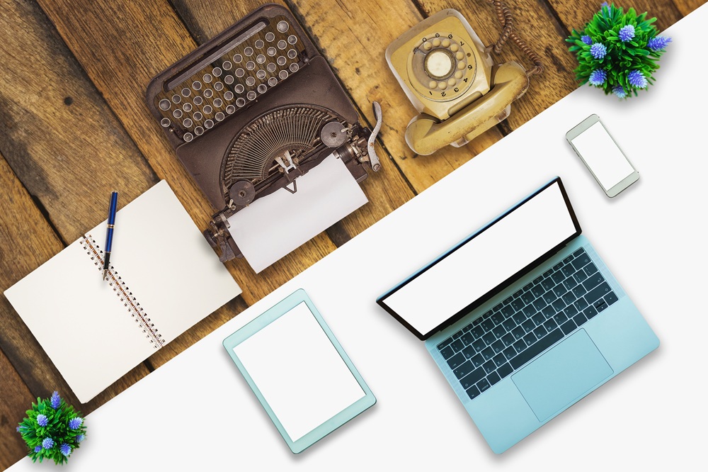 Old typewriter and rotary dial phone pictured next to laptop, tablet and mobile phone. Credit: Shutterstock.