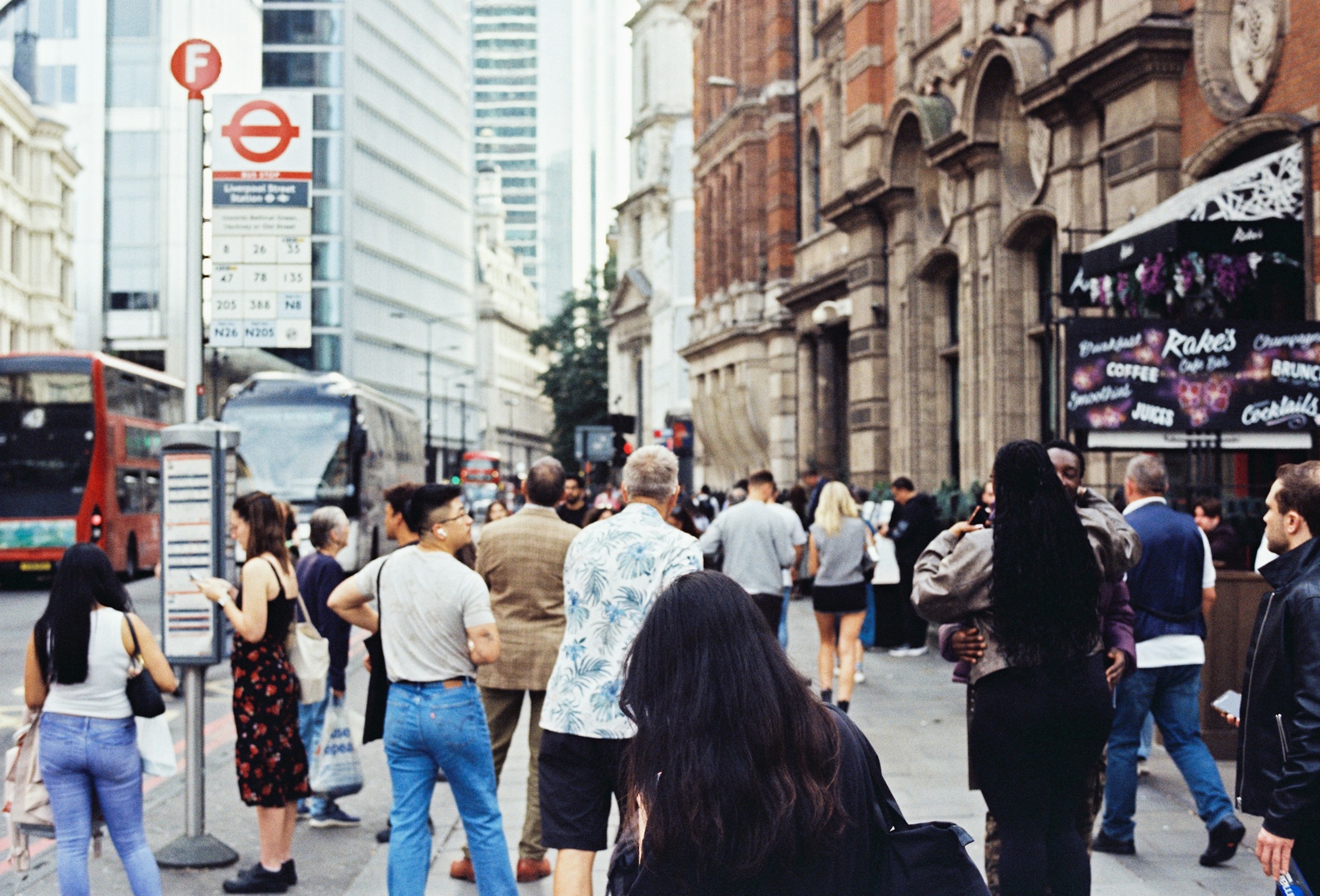 Crowds of people in a central London street, standing near a bus stop. A red bus passes by. Credit: Lawrence Krowdeed, Unsplash.