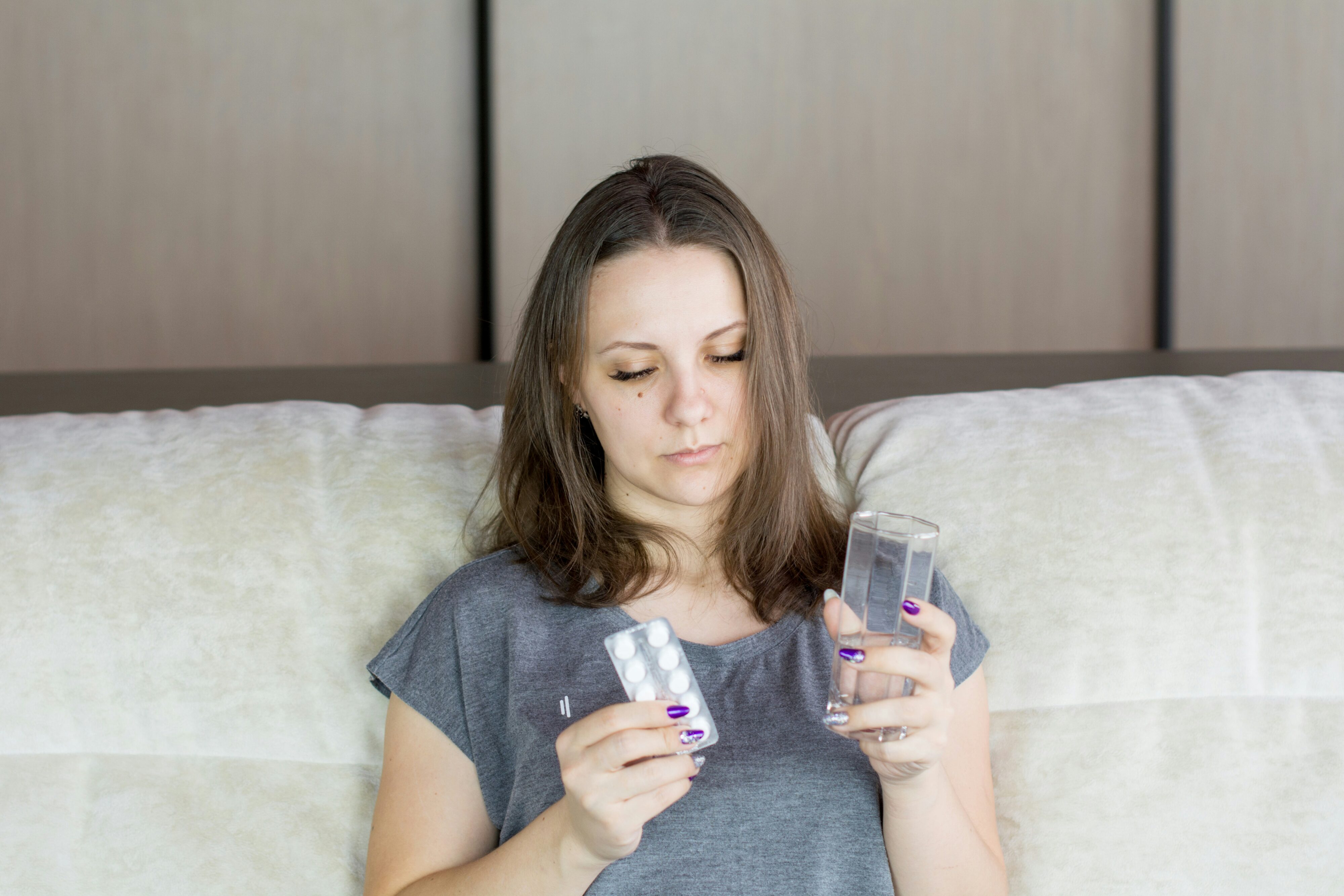 Woman on sofa holding packet of pills and a glass of water. Credit: Bermix Studio, Unsplash.