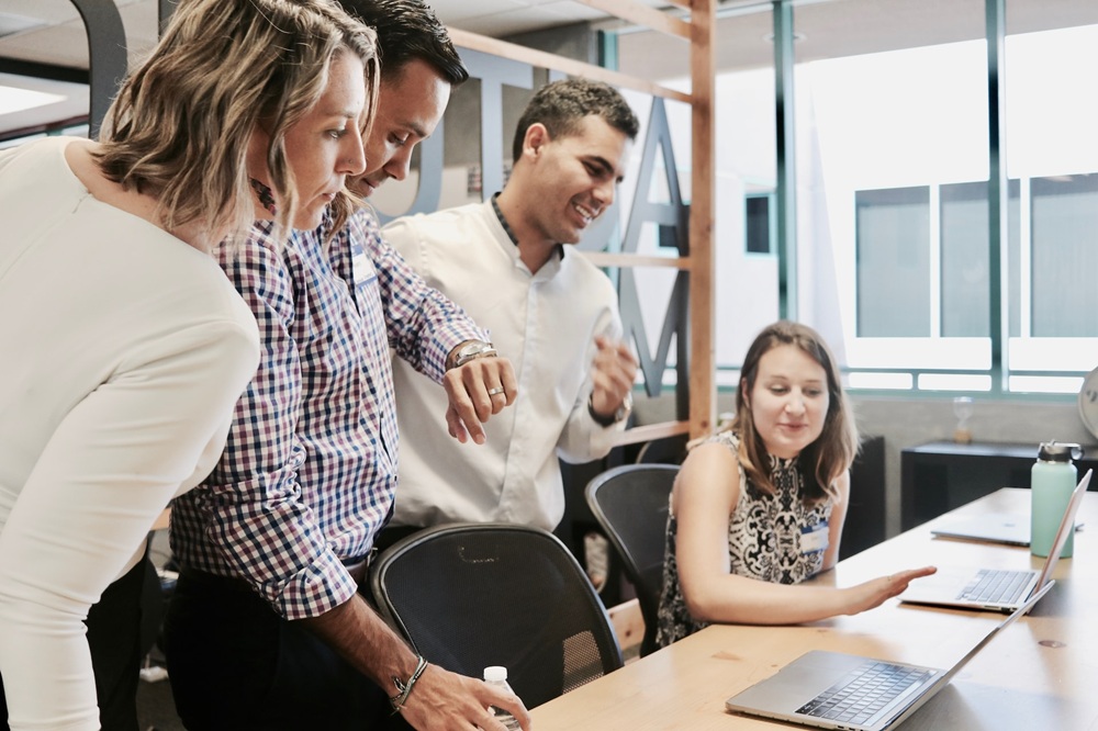 Team of 4 people in an office looking at info on a laptop. Credit: Unsplash